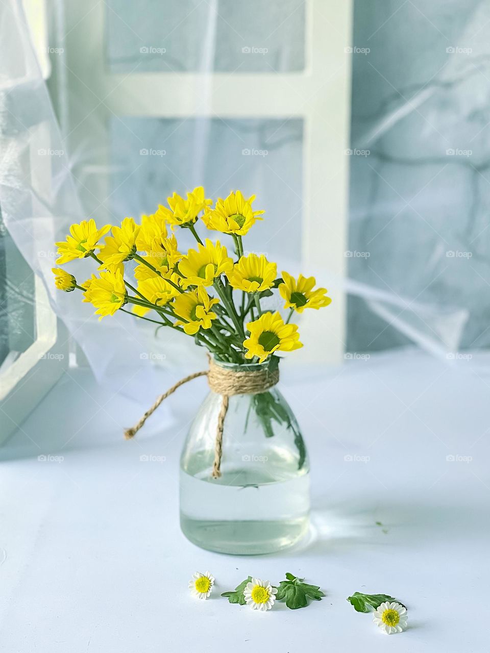 Yellow blooming daisies in a glass jar with white ambiance around it