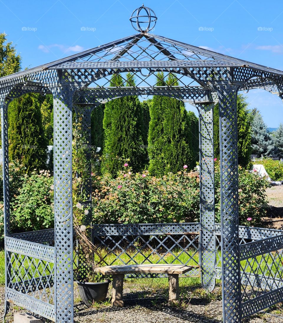 outdoor gazebo in a bright Summer garden center setting with a stone bench to sit on inside and enjoy the quiet