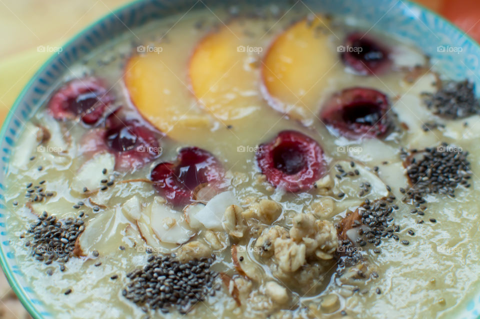 Closeup of beautiful fruit smoothie bowl with sliced fruit garnish decoration of halved black cherries, sliced peach, oatmeal, chia seed, coconut, almonds and chia seed