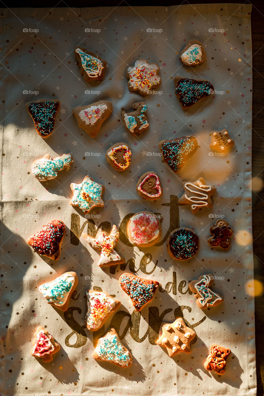 Christmas gingerbread cookies in many shapes decorated with colorful frosting, sprinkle, icing, chocolate coating, toppers, put on plain fabric