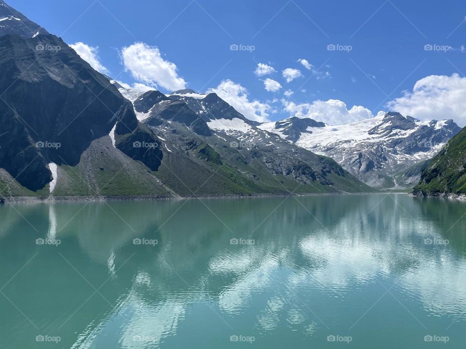 Beautiful mountains and snow covered mountain peaks and glaciers by the lake at Mooserboden reservoir Austria on a sunny day 