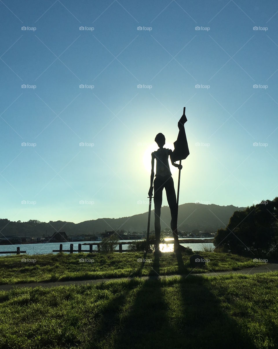 A sculpture of a woman warrior stands in the sun