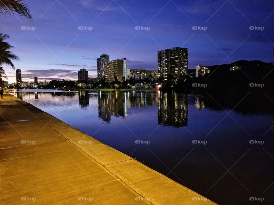 Skyline with water in Honolulu Hawaii. Beautiful reflection of lights and buildings in the water, near a river walk. Sunset of Hawaii, vacation.