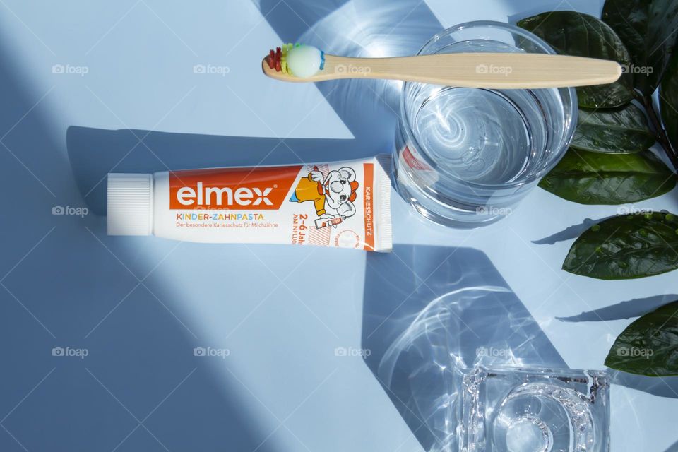 Elmex toothpaste for small children for oral and dental care, ecological toothbrush is on a blue background, with water, and a green flower.