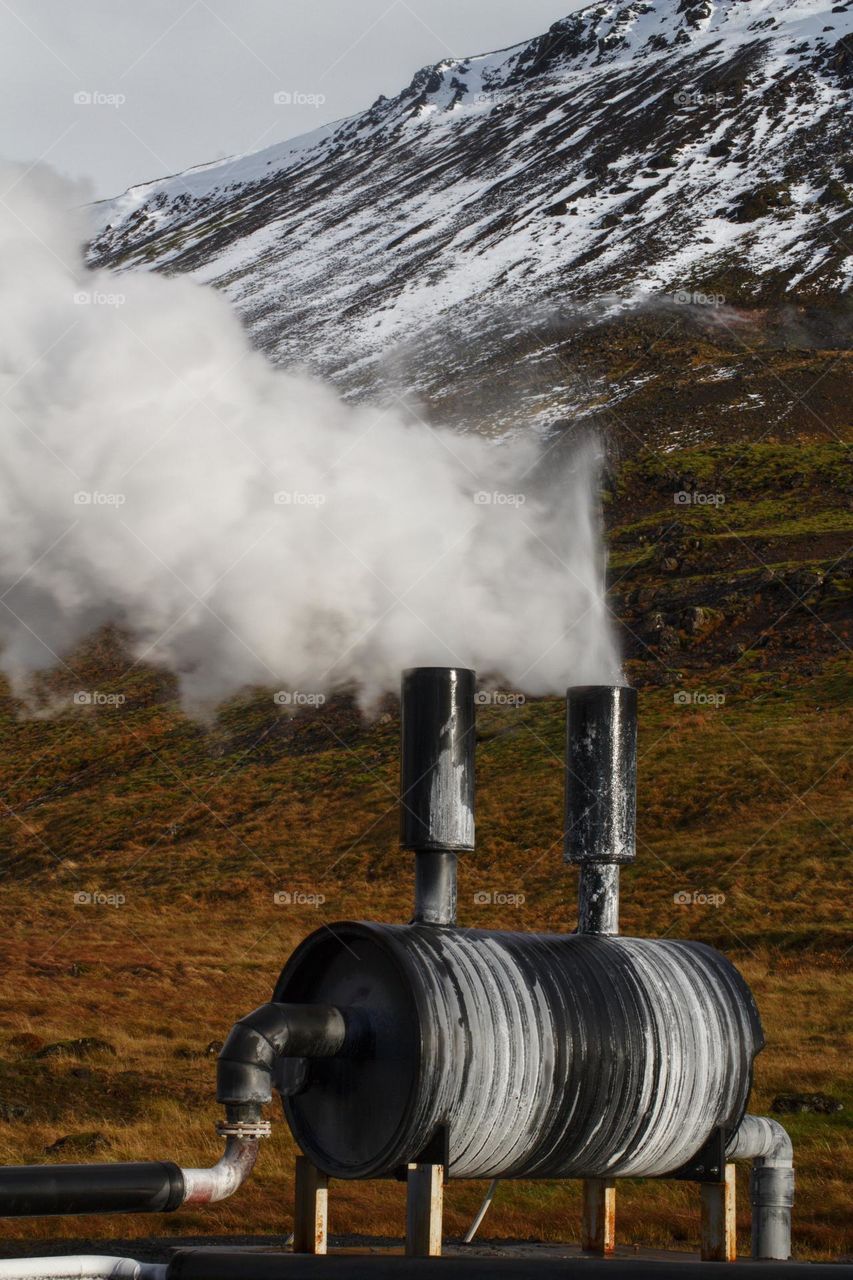 Steam generating device in Iceland on the backdrop of snow-covered mountains.