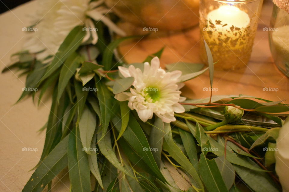 A white mum is placed among willow and eucalyptus in a romantic wedding centre piece wreath. A lit votive adds romance to this image. 