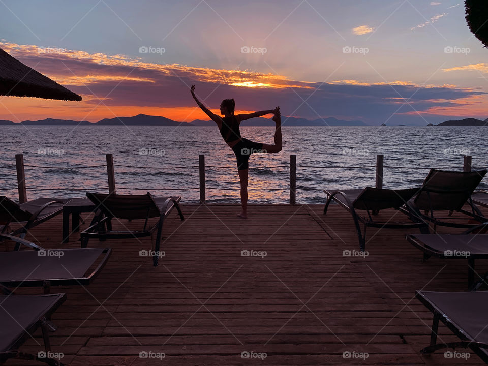 Silhouette of a young woman doing yoga outdoor at purple sunset at the seaside 