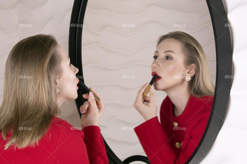 The girl paints her lips with red lipstick