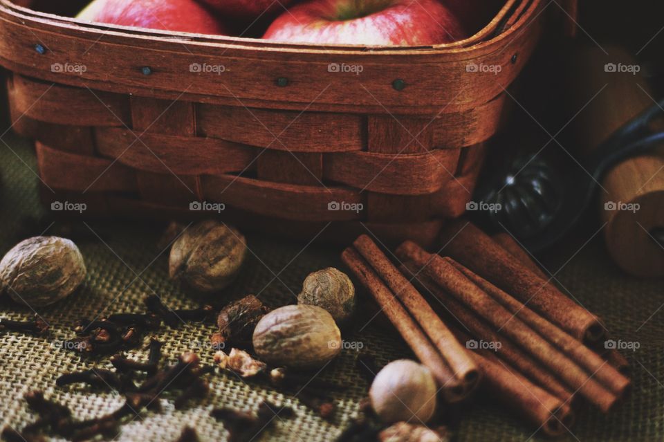 Cinnamon sticks, whole nutmeg, whole cloves, a vintage pie crust crimper, a wooden pastry roller and apples in a basket on burlap