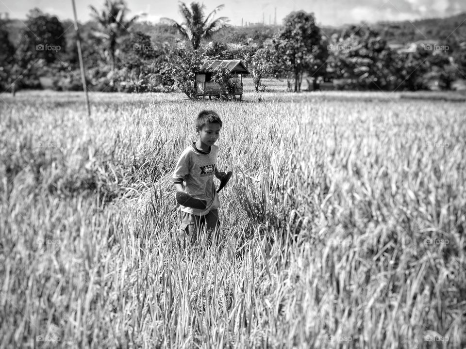 Boy holding flip-flops in hand at field