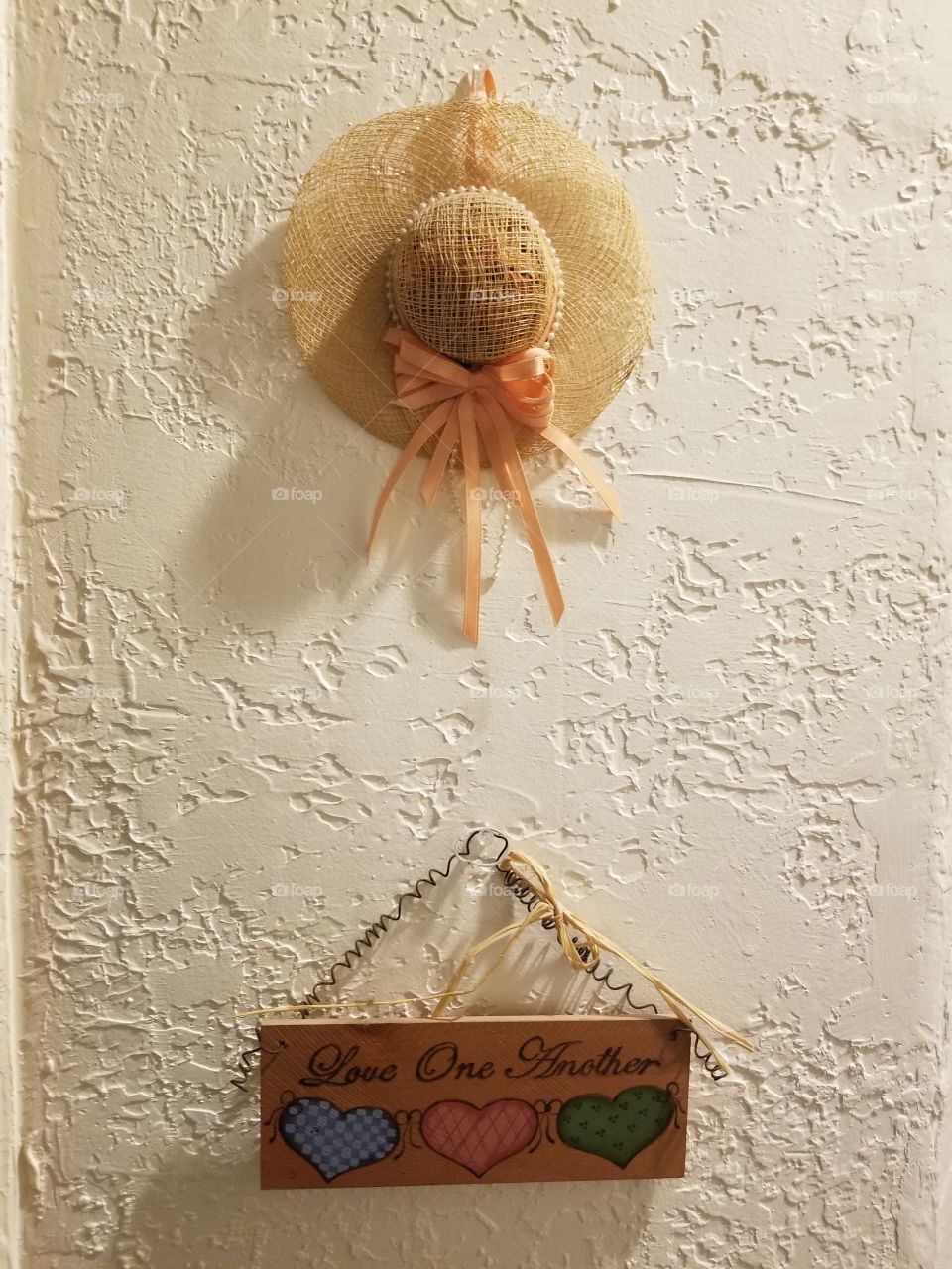 wall grouping of a sign and decorative hat, sign reads "love one another" in colorful hearts. simple decoration