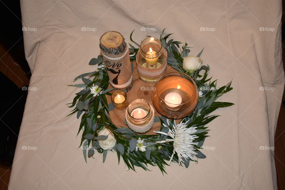 A romantic arrangement as a wedding centre piece. A willow wreath with eucalyptus and white flowers compliments the natural wood table number sign and gold and burlap accented glass candle holders. Warm, romantic and ready to edit. 