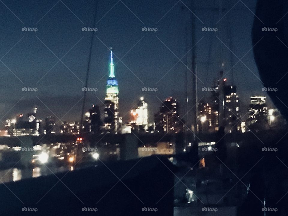 A New York cityscape as seen from our sailboat, the “Salvation” looking beyond the Pulaski Bridge in the foreground onto parts of Long Island City, Queens and Manhattan including the lit up Empire State Building. Photo from 2018. Hypnotic Productions