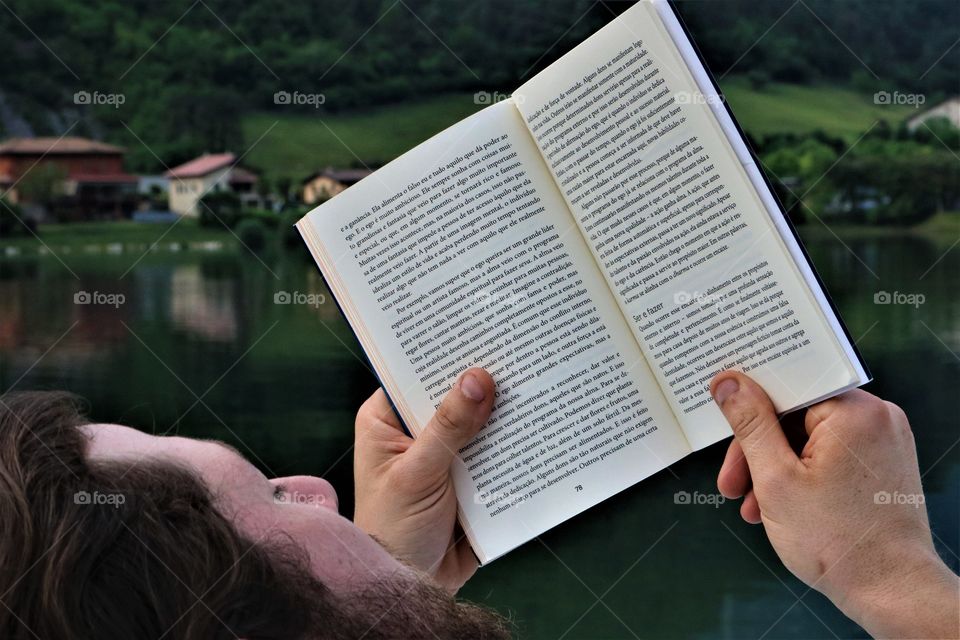 blond man reading a book in front of the beautiful landscape of lake and houses, in evidence the book.