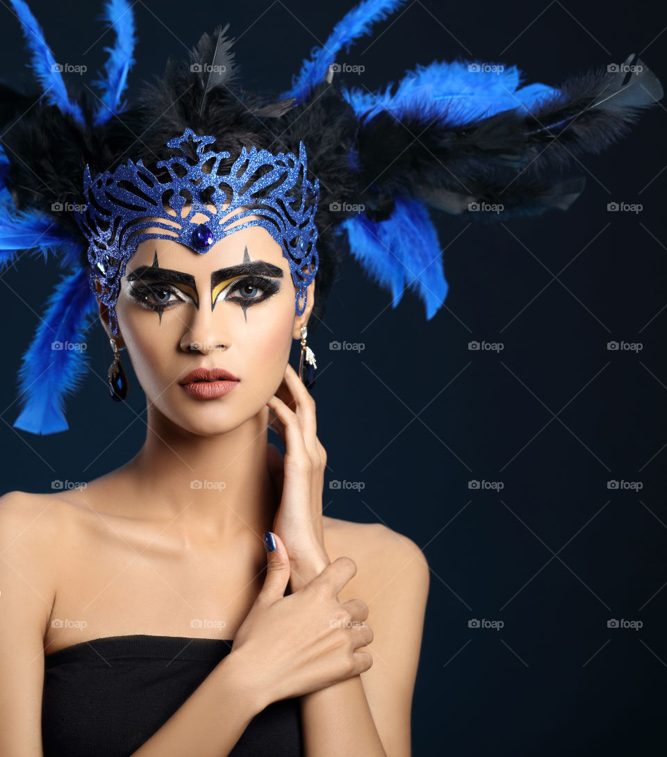 Young woman wearing blue feather crown with eye makeup