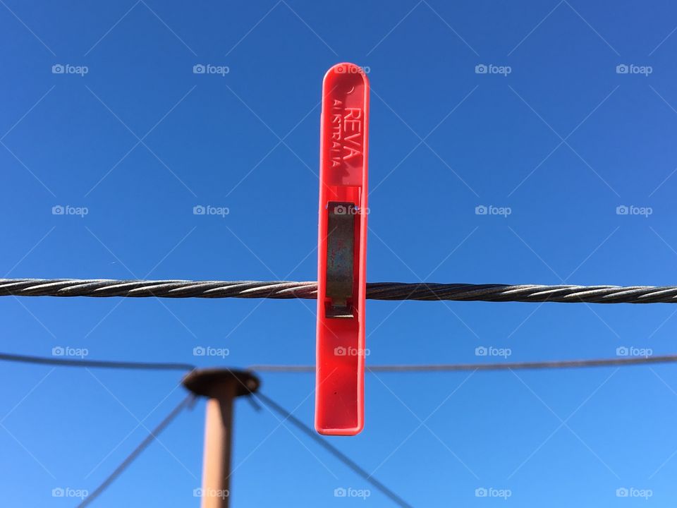 Bright Red clothespin on a wire clothesline against a vivid blue sky