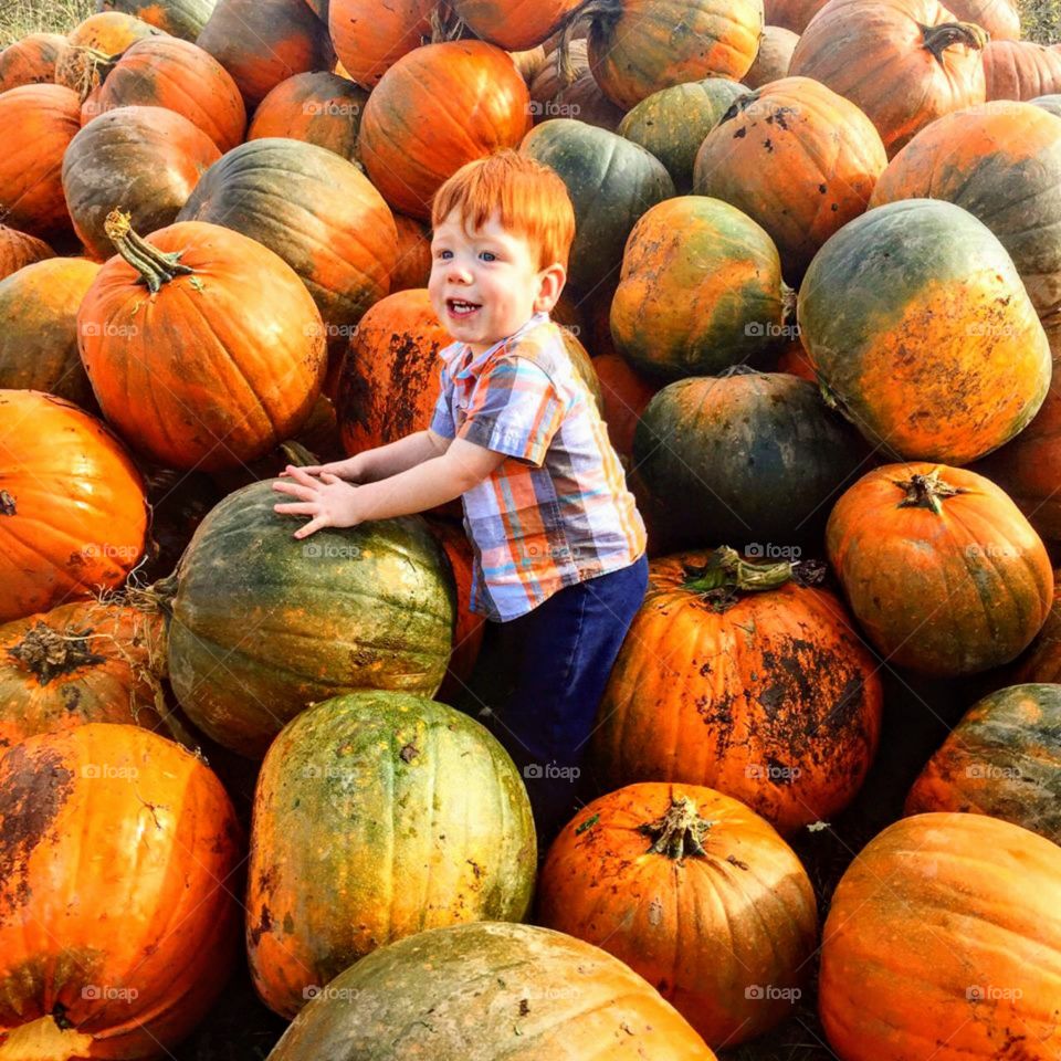 Red haired toddler in stack of pumpkins. 