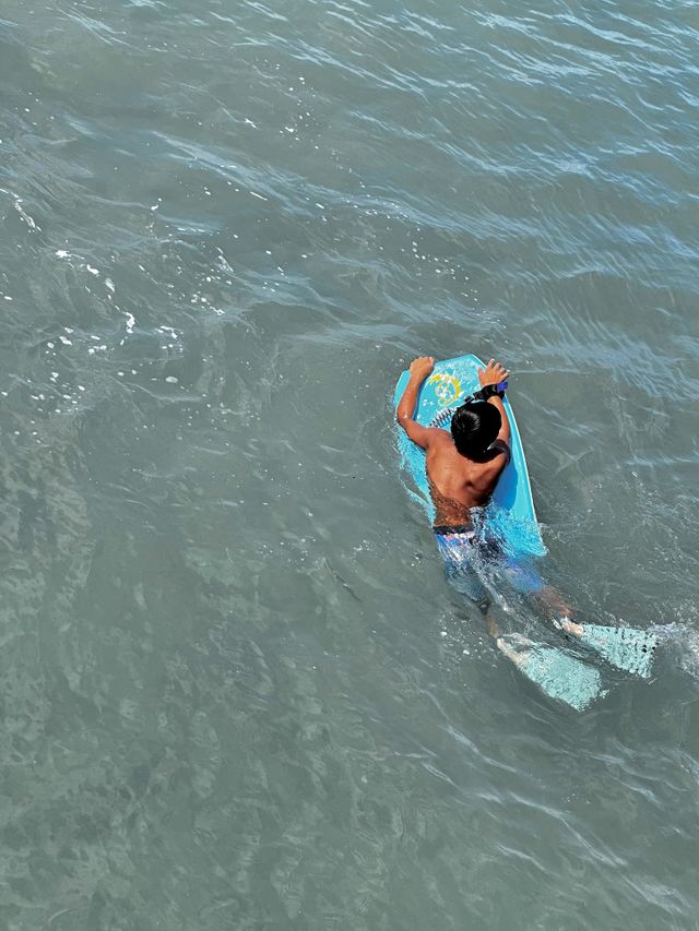 A boy on an aqua boogie board wearing a coiled wrist leash and aqua colored fins maneuvering to catch his next wave in Hawaii 