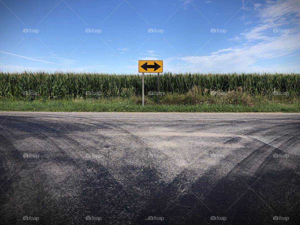 Turning sign on a country road by a corn field