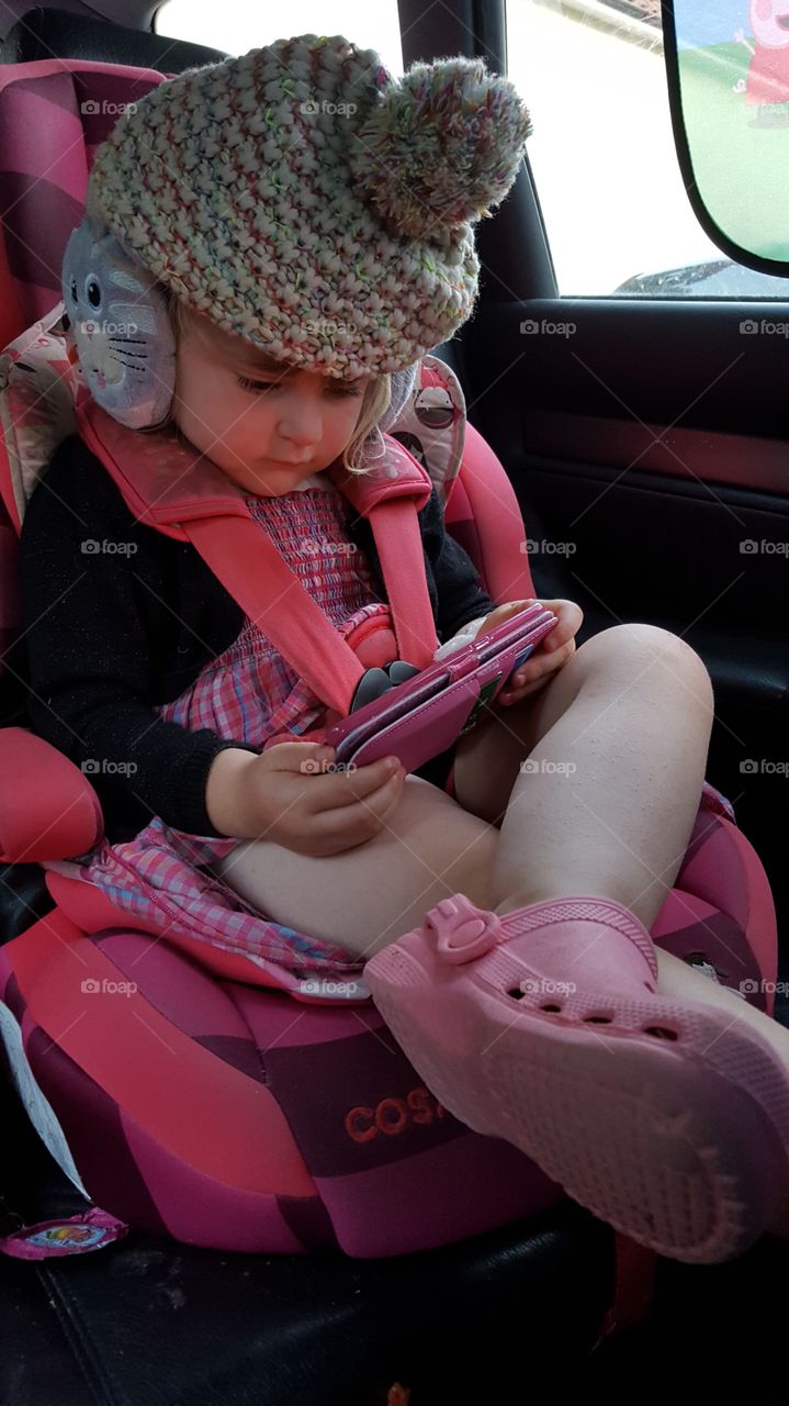 Four Year Old Girl Playing Games on 'Phone in a Car Seat