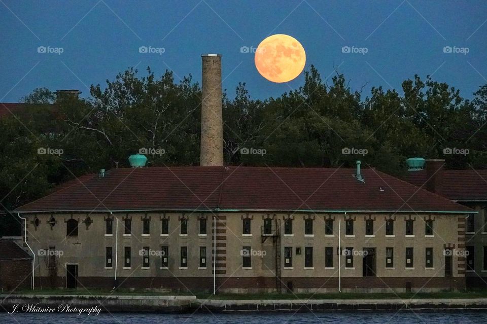 A full moon rises above a historic complex in New York City as seen from Liberty park in New Jersey