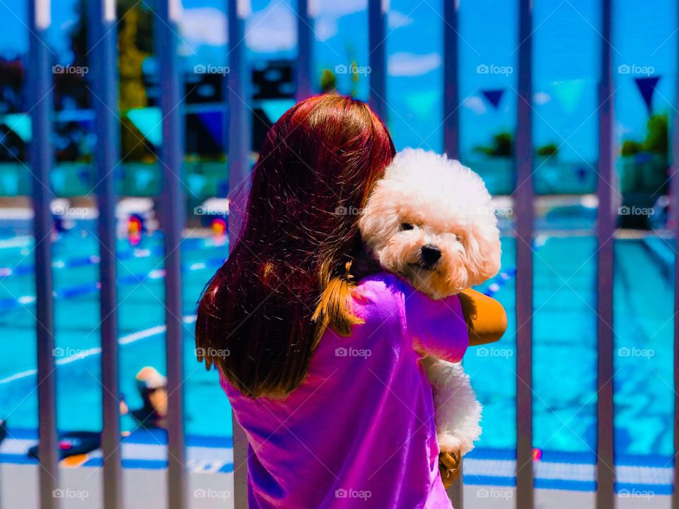 Vitality! Colors galore in this shot of a red head girl holding a puppy by a competitive lap pool. Flags in the distance. Turquoise, magenta, Auburn, aqua...
