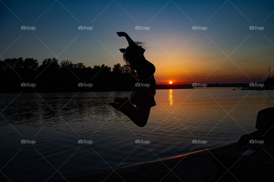 A woman jump and having fun into the air into the sunset a sunnye day. It just a silouetts against the night