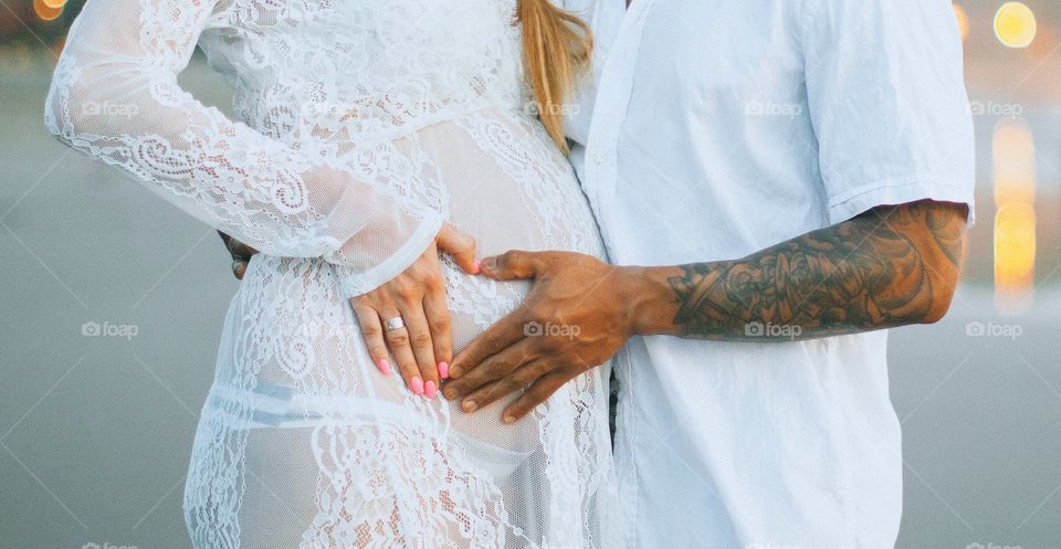 Tender and sensual photo on the beach. White dress emphasize the belly, husband hands show the love. Best photosession for our son 