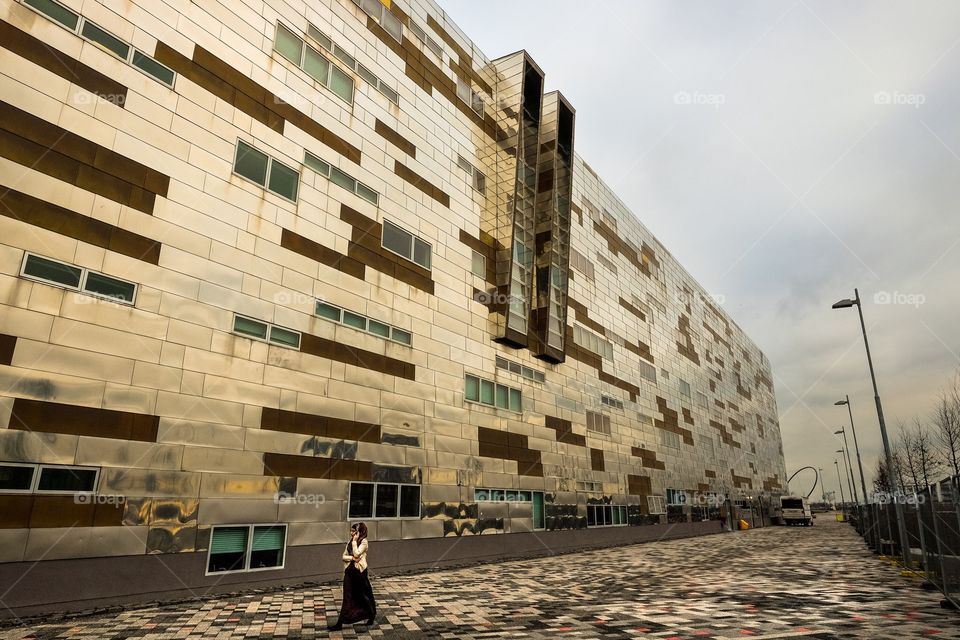 In the City. A young woman is dwarfed by a huge modern building as she talks on a phone in the city. 