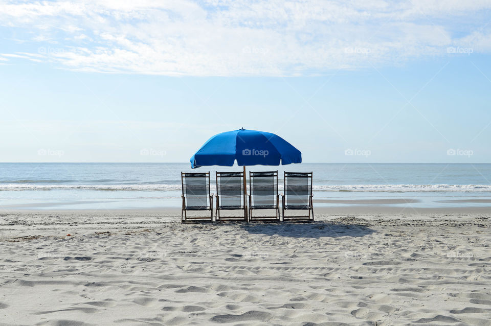 Lounge chairs lined up with an umbrella on the beach overlooking the ocean