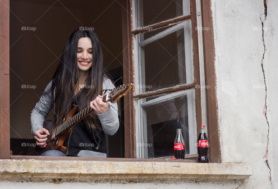 Beautiful woman playing a guitar on the window, Coca-Cola bottle beside her