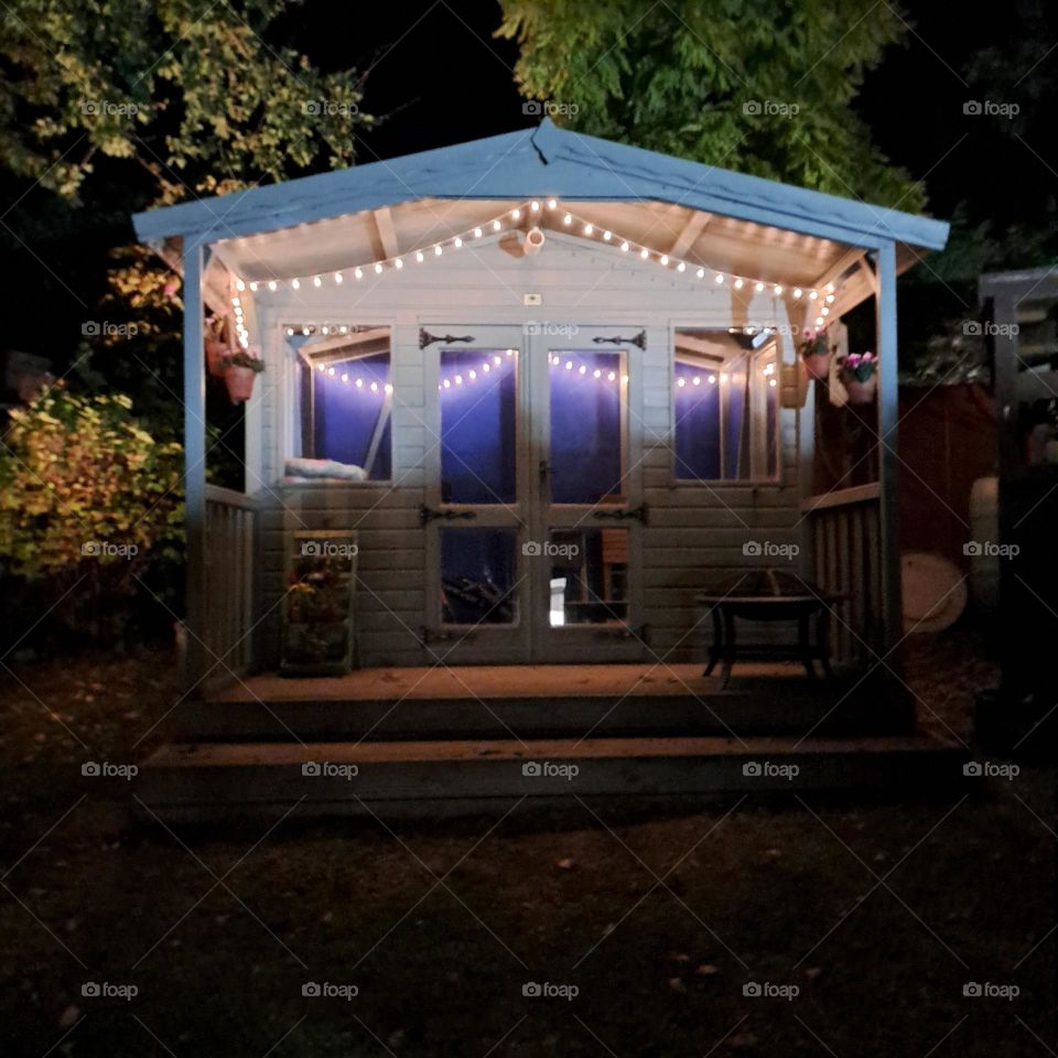 soft lighting in dark. fairylights over garden summerhouse. shadows casting. trees lit up. night.