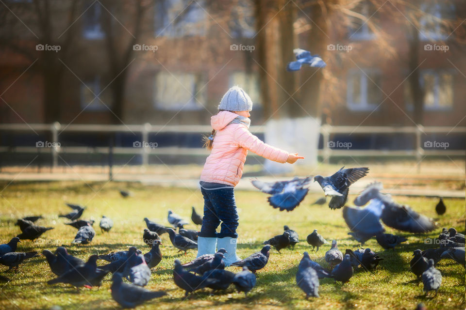 Little girl with pigeons in spring park.