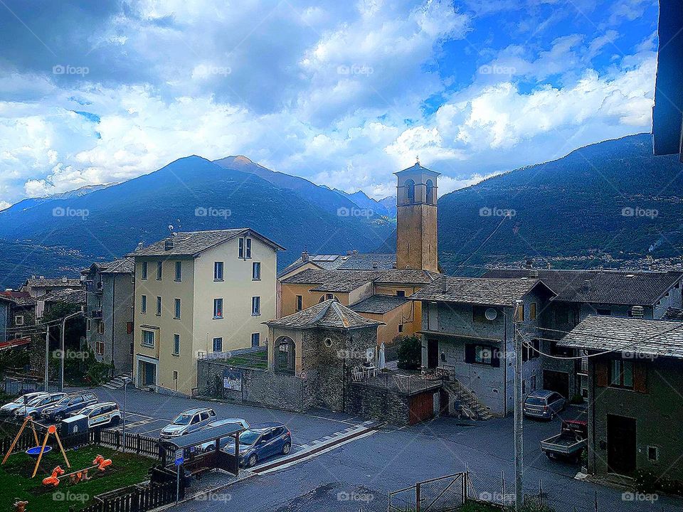 Village.  View of the small settlement of Faedo Valtellino.  Italy.  In the background are the Alps mountains that touch the blue sky with white-gray clouds.