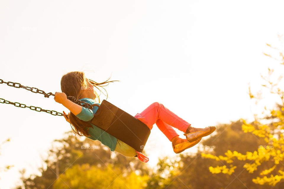 Memories of summer - girl swinging at sunset with trees in the background