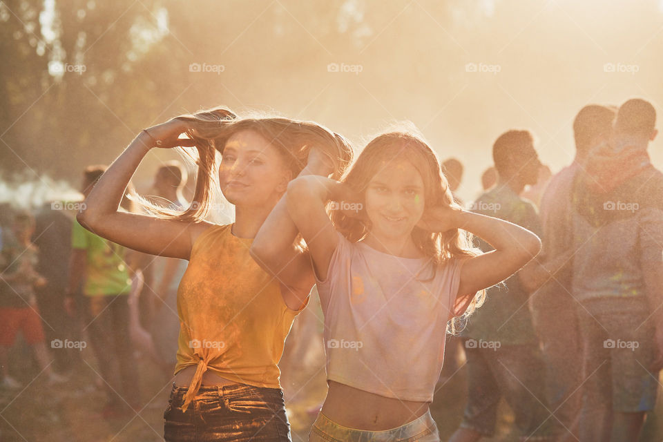 Portrait of happy smiling young girls with colorful paints on faces and clothes. Two friends spending time on holi color festival