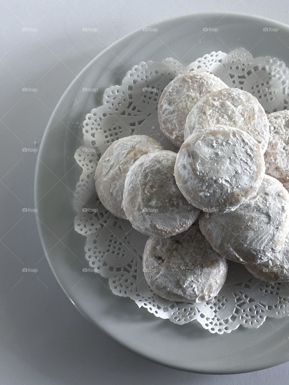 A stack of Mexican wedding shortbread cookies on a white paper doily placed on a swirl design ceramic white plate on white background 