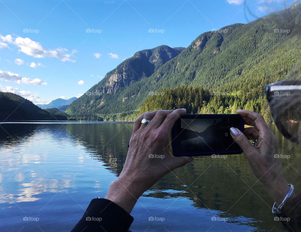 Woman photographing with smartphone beautiful scenic mountain lake