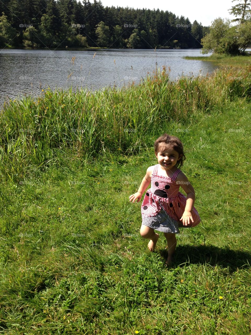 Little girl walking on grass near lake