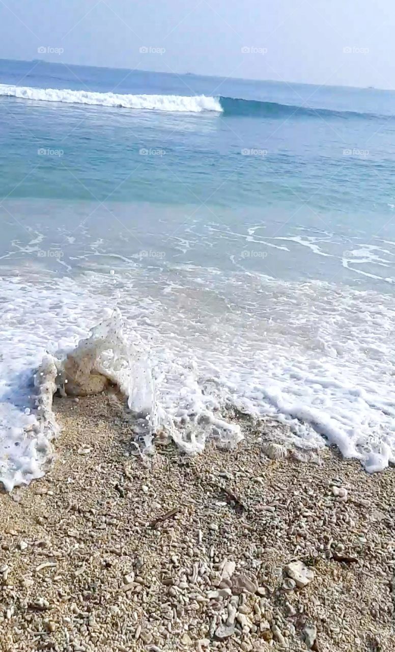 white sea foam and sand in small waves on blue sea background. close up