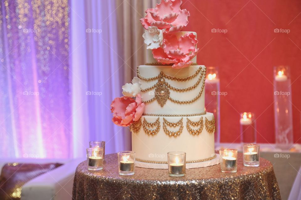 A fancy cake with massive pink flowers and decorated in gold
