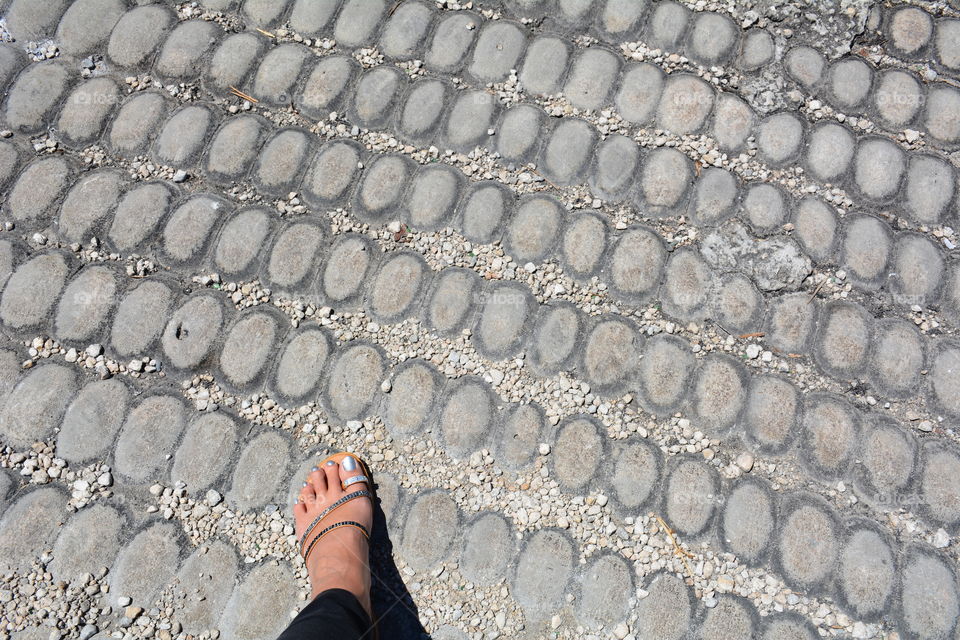 Female foot in sandal stepping into patterned pavement