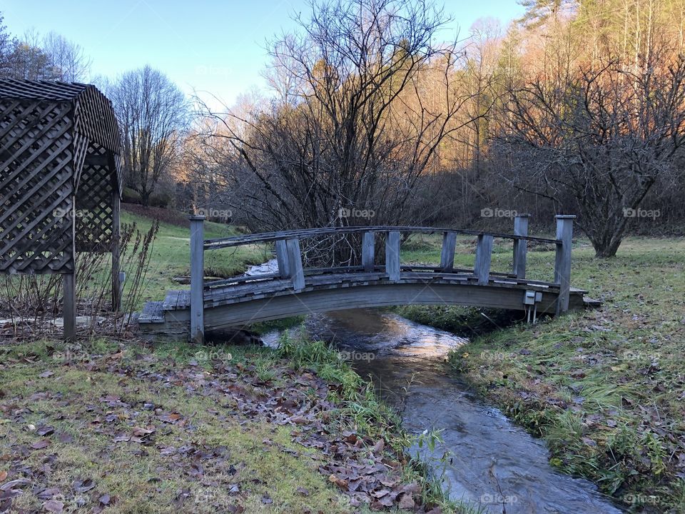 North Georgia stream cutting a natural path- passes under an arc wooden bridge, delivering clear, fresh, cold mountain waters to neighboring wildlife.