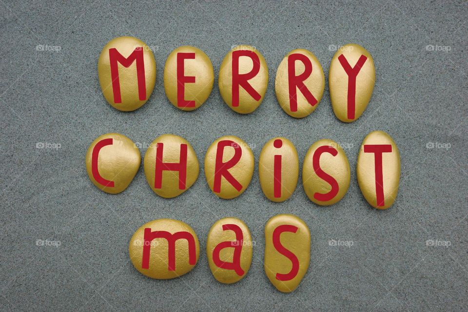 Merry Christmas text composed with hand painted yellow and red stones over green sand