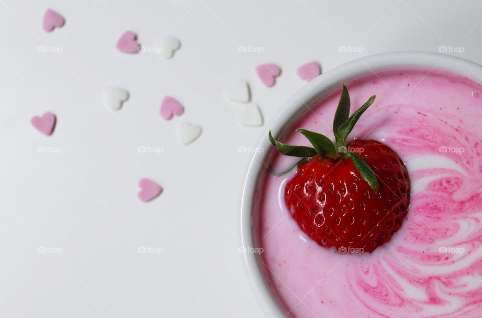 Strawberry yogurt with fresh strawberry on a white table decorated with white and baby pink sweet hearts