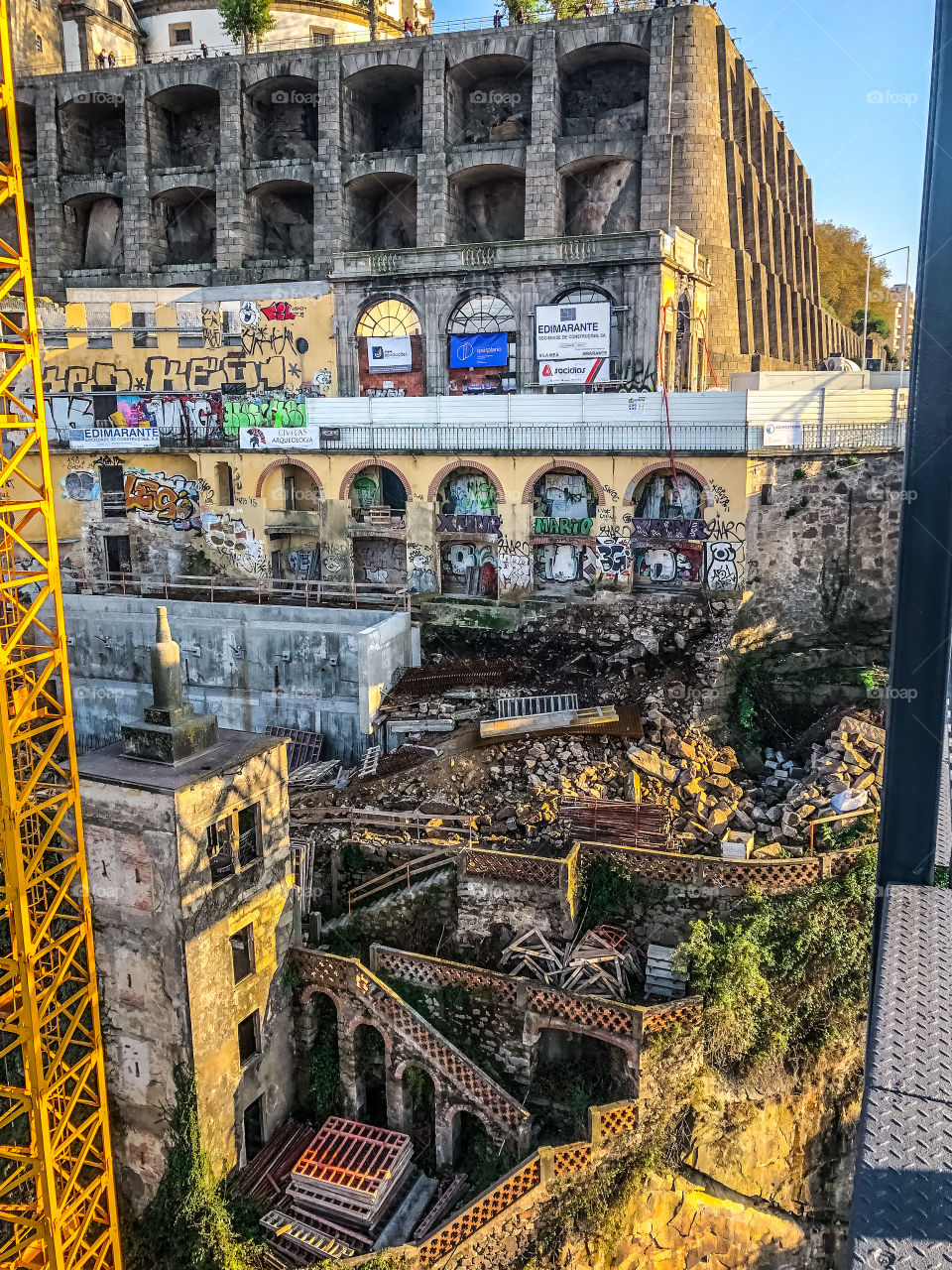 A scene of demolition and dereliction in Porto, framed by the metal structures of a crane and a bridge on either side