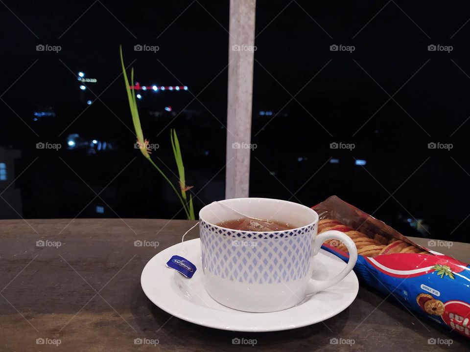 Bandung, Indonesia - February 28, 2022: a cup of hot tea and biscuits on the balcony at night. Enjoy the view of city lights. Relax time