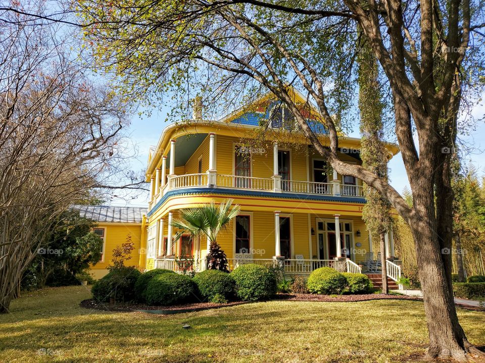 Yellow historic two story home with second floor exterior wrap around balcony