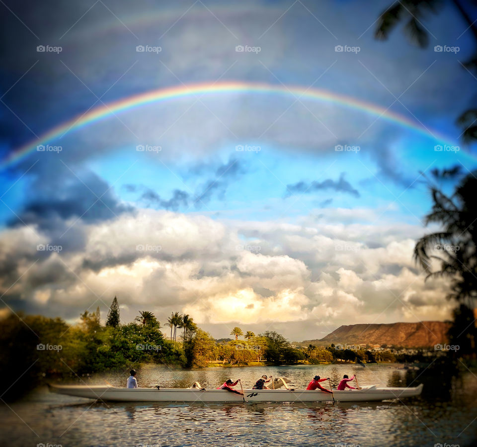 Outrigger paddlers on the Ala Wai Canal in Honolulu with Diamond Head in the distance and a rainbow overhead
