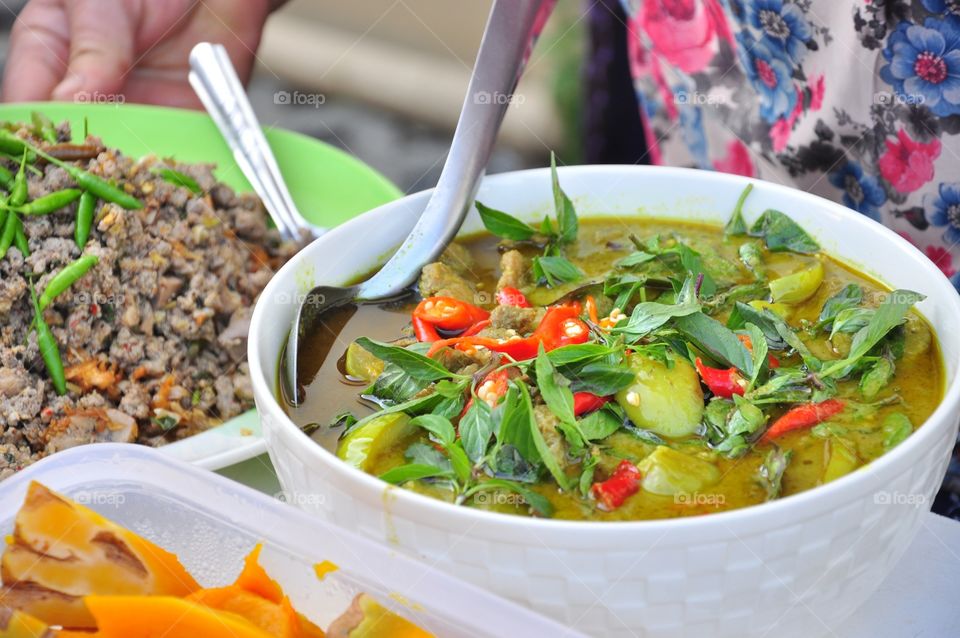 Green curry with a ladle beside. There are Thai basils and spur peppers on it. 